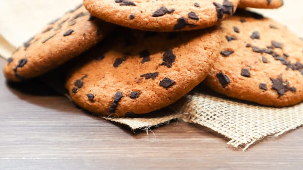 American chocolate chip cookies on a brown wooden table and on a linen napkin close-up. Traditional rounded crunchy dough with chocolate chips. Bakery. Delicious dessert, pastries. Rural still life