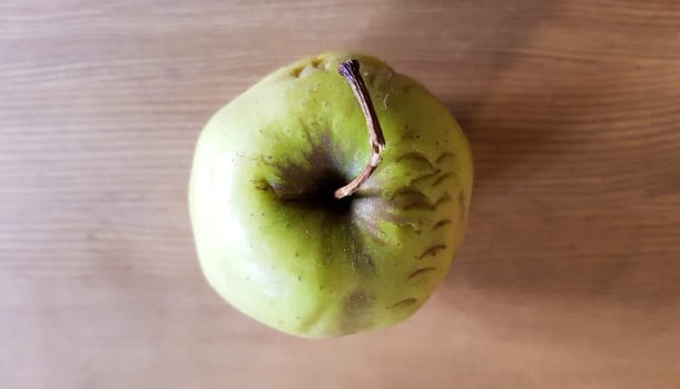 green rotten apple on a wood background. Green apple on a old wooden background, top view. Organic juicy bio apple ugly, with defects edible lies on a wooden table. No ugly food.