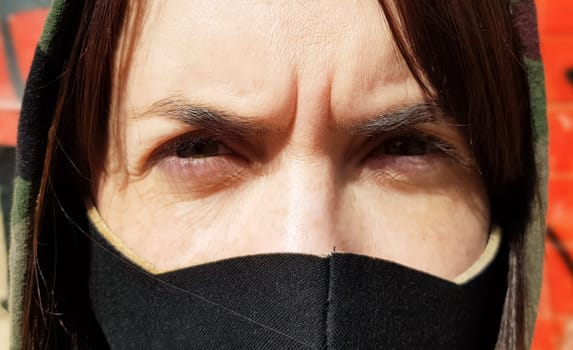 Portrait of a woman in a protective black mask outdoors near an old broken wall. Coronavirus and air pollution concept. A girl wears a protective mask to protect against a pandemic