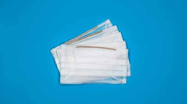 Three disposable surgical face masks with rubber pads to cover the mouth and nose on a blue background. The concept of protection from bacteria, healthcare and medicine. COVID-19. Copy space.