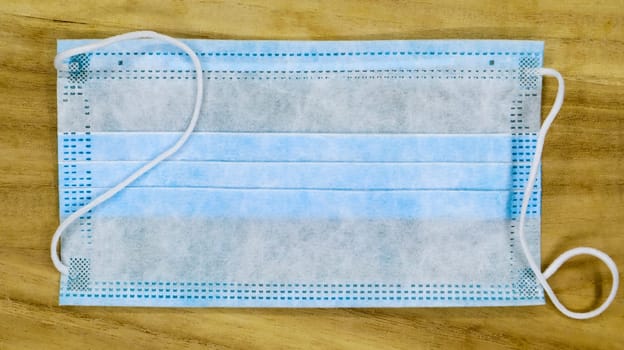 One 3-ply disposable surgical face mask with rubber pads covering the mouth and nose on a wooden table. The concept of protection from bacteria, healthcare and medicine. COVID-19. Dangerous virus
