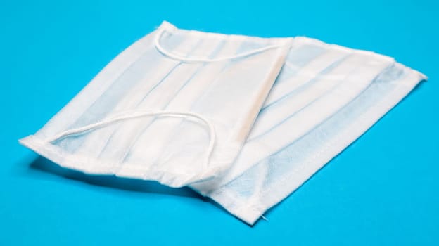 Two three-layer disposable surgical face masks with rubber pads to cover the mouth and nose against a blue background. The concept of protection from bacteria, healthcare and medicine. COVID-19
