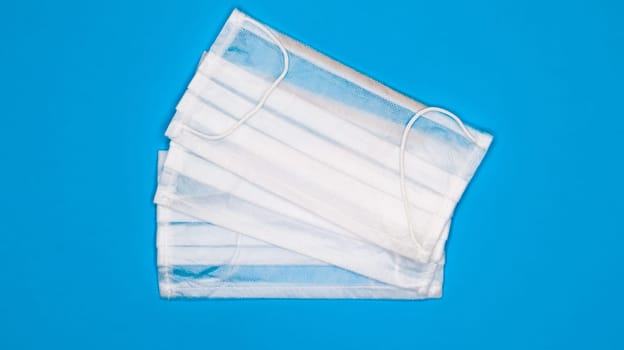 Two three-layer disposable surgical face masks with rubber pads to cover the mouth and nose against a blue background. The concept of protection from bacteria, healthcare and medicine. COVID-19