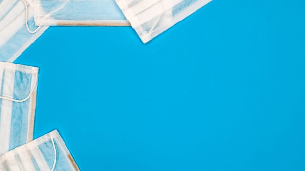Many antiviral protective medical face masks with earloops are set against a blue background. Surgical mask background. Respiratory syndrome, coronavirus disease COVID-19. Copy space.