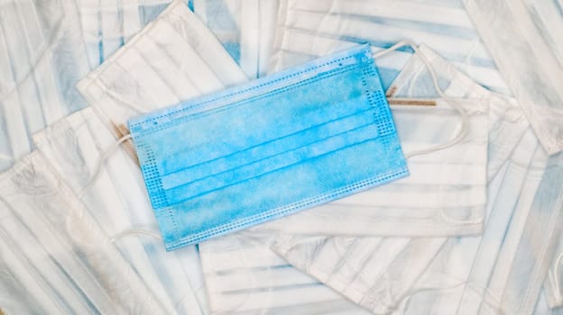 Coronavirus protection. Many antiviral protective medical face masks with ear loops spread out on a blue background. Surgical mask background. Respiratory syndrome, coronavirus disease COVID-19