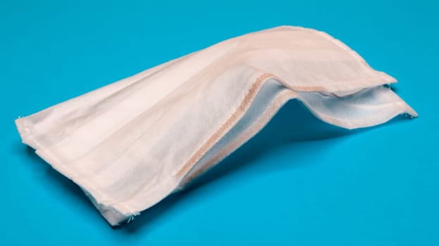 Two three-layer disposable surgical face masks with rubber pads to cover the mouth and nose against a blue background. The concept of protection from bacteria, healthcare and medicine. COVID-19.