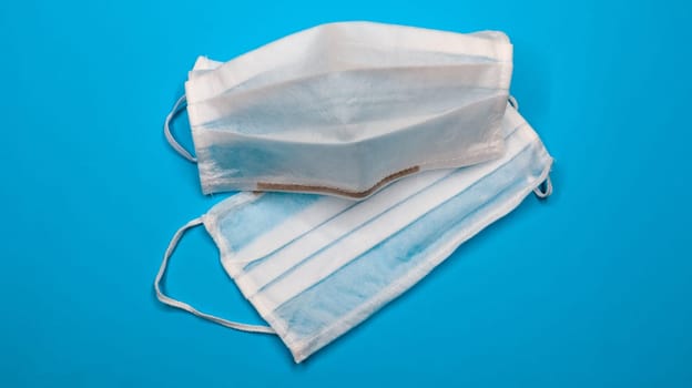 Two disposable surgical face masks with rubber pads to cover the mouth and nose on a blue background. The concept of protection from bacteria, healthcare and medicine. COVID-19. Copy space.
