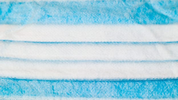 One 3-ply disposable surgical face mask close-up with rubber pads covering mouth and nose against blue background. The concept of protection from bacteria, healthcare and medicine. COVID-19