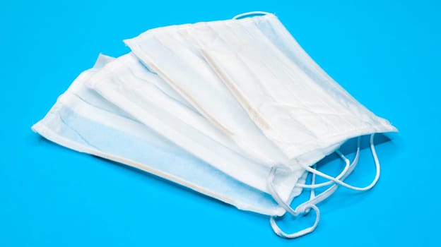 Three disposable surgical face masks with rubber pads to cover the mouth and nose on a blue background. The concept of protection from bacteria, healthcare and medicine. COVID-19. Dangerous virus.