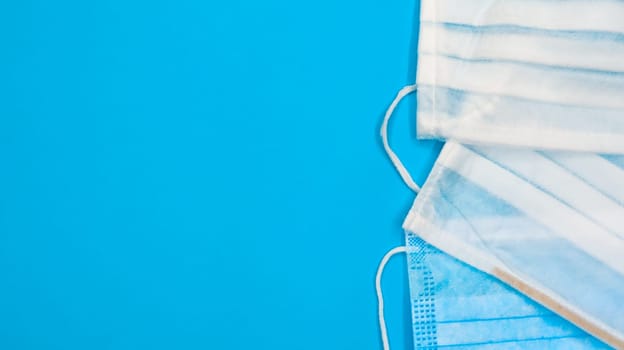 Three disposable surgical face masks with rubber pads to cover the mouth and nose on a blue background. The concept of protection from bacteria, healthcare and medicine. COVID-19. Copy space.