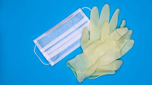 A pair of disposable latex medical gloves and a surgical mask on a blue background. Covid-19 virus protection concept. Protective items. Means of protection