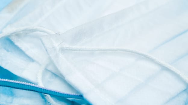 Coronavirus protection. Many antiviral protective medical face masks with ear loops spread out on a blue background. Surgical mask background. Respiratory syndrome, coronavirus disease COVID-19
