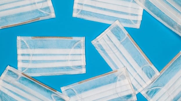 Coronavirus protection. Many antiviral protective medical face masks with ear loops spread out on a blue background. Surgical mask background. Respiratory syndrome, coronavirus disease COVID-19