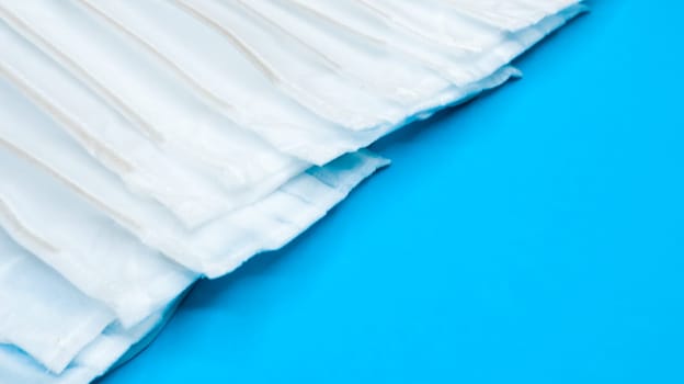 Many antiviral protective medical face masks with earloops are set against a blue background. Surgical mask background. Respiratory syndrome, coronavirus disease COVID-19. Copy space.