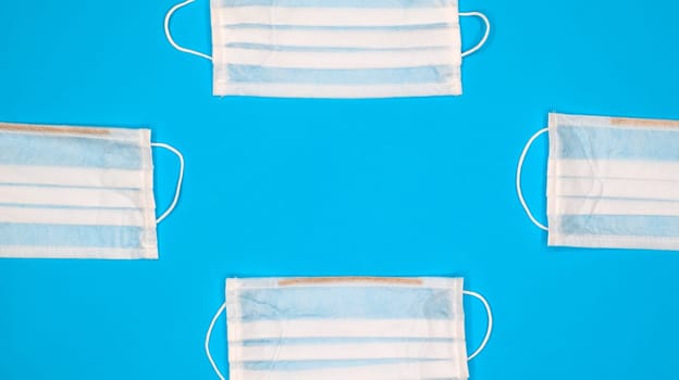 Many antiviral protective medical face masks with earloops are set against a blue background. Surgical mask background. Respiratory syndrome, coronavirus disease COVID-19. Copy space.