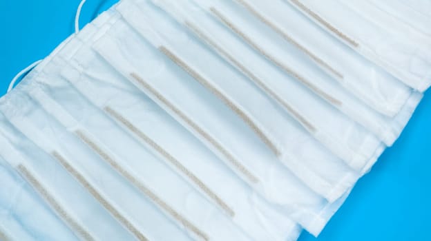Coronavirus protection. Many antiviral protective medical face masks with ear loops spread out on a blue background. Surgical mask background. Respiratory syndrome, coronavirus disease COVID-19