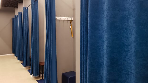 Boutique interior, fitting room in a shopping center. Nobody. Empty fitting rooms with blue curtains and gray walls and a large mirror. Dressing rooms in a clothing store without people