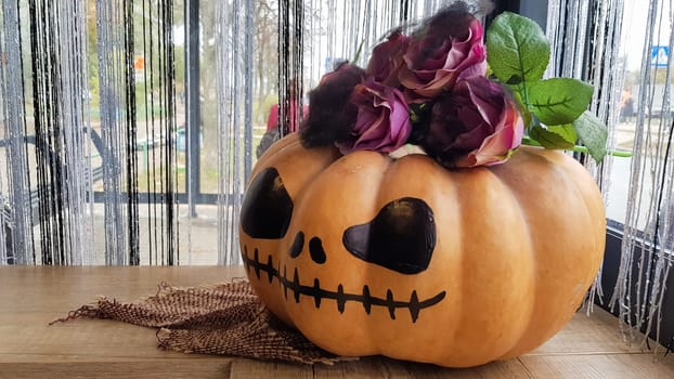 Pumpkin with a scary face on a wooden table. The interior of the house is decorated with pumpkins and spider webs for the holiday of Halloween