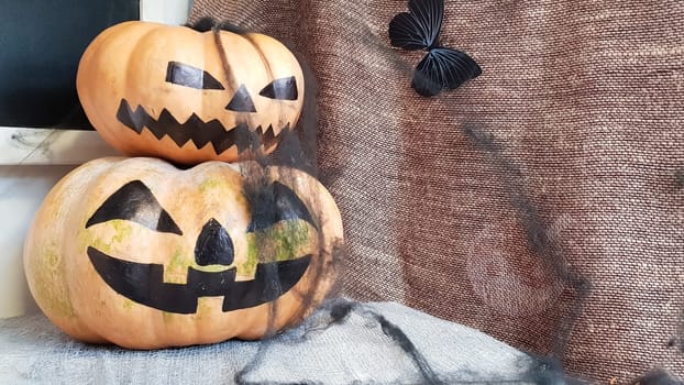 Pumpkin with a scary face on a wooden table. The interior of the house is decorated with pumpkins and spider webs for the holiday of Halloween