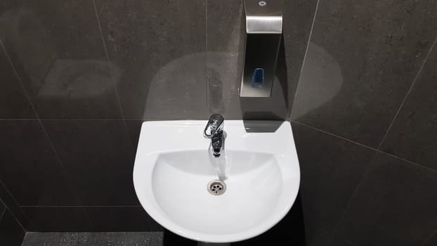 white ceramic washbasin with chrome faucet in the toilet with gray tile.