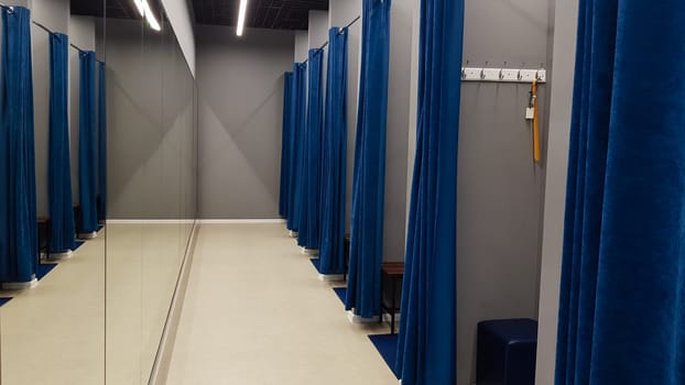 Boutique interior, fitting room in a shopping center. Nobody. Empty fitting rooms with blue curtains and gray walls and a large mirror. Dressing rooms in a clothing store without people