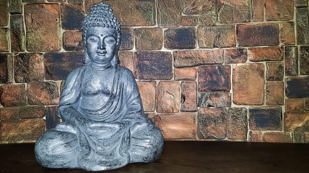 Ukraine, Kiev - June 10, 2020. Statuette of the blessing of Buddha on a wooden shelf against a stone wall. Ceramic figurines and figurines decoration or symbol in the home interior