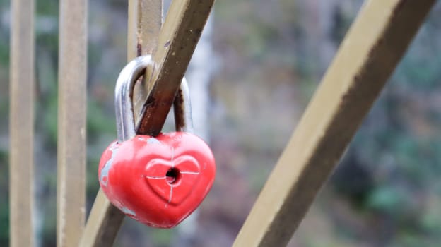Shabby red lock in the shape of a heart. Valentine's day love concept. A padlock hanging on a metal railing is a sign of eternal love. The tradition of hooking a castle with a fence.