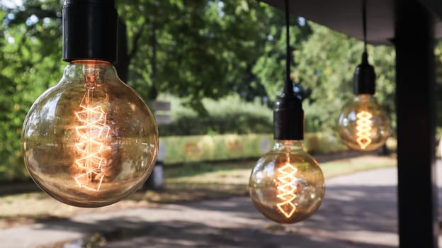 Edison incandescent bulbs hang in a retro loft style. Cafeteria decoration close-up. Street decor Light lanterns Warm light. Soft focus, blurred street background.