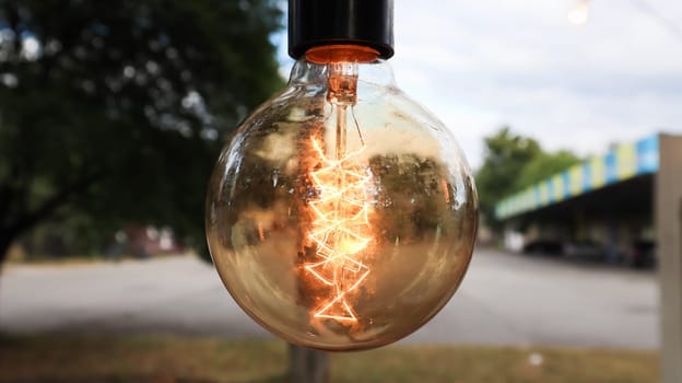 Edison incandescent bulbs hang in a retro loft style. Cafeteria decoration close-up. Street decor Light lanterns Warm light. Soft focus, blurred street background.