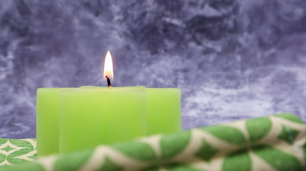 Composition with one green lit candle on a table with a green linen napkin against a beautiful gray marble background. Place for your text. Christmas decorations