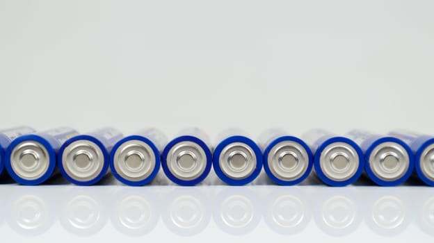 Lots of AA alkaline batteries on a white glossy background with reflection with copy space lined up in one line