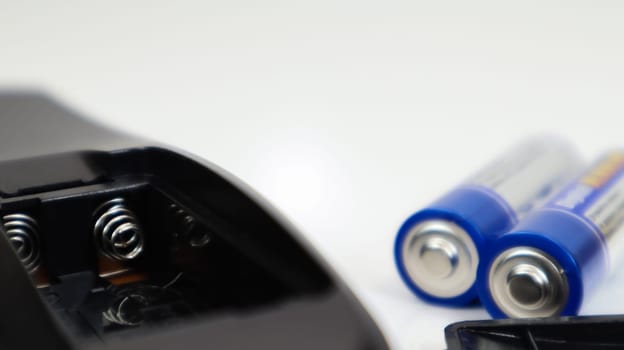 Black remote control with blue AAA batteries on a white background. Battery replacement, spare parts. Battery empty compartment of the remote control close-up