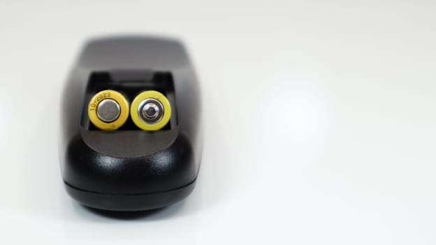 Black remote control with yellow AAA batteries on a white background. Battery replacement, spare parts. Remote control battery compartment close-up. Copy space.