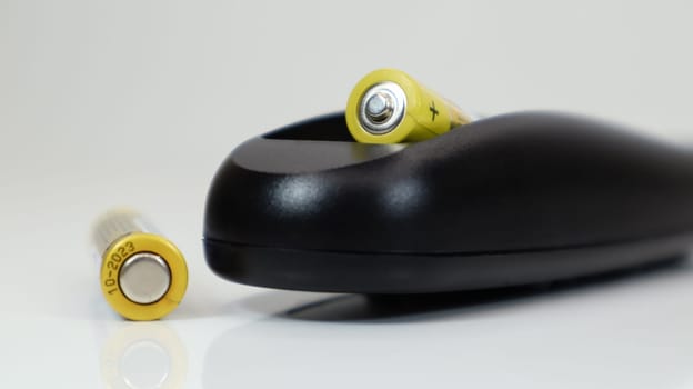 Black remote control with yellow AAA batteries on a white background. Battery replacement, spare parts. Remote control battery compartment close-up