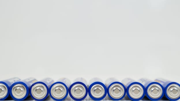 Lots of AA alkaline batteries on a white glossy background with reflection with copy space lined up in one line. Ukraine, Kiev - January 7, 2021
