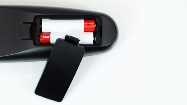 Black TV remote control with AAA alkaline batteries in red and white on a white background. Battery replacement, spare parts. Remote control battery compartment close-up. Copy space