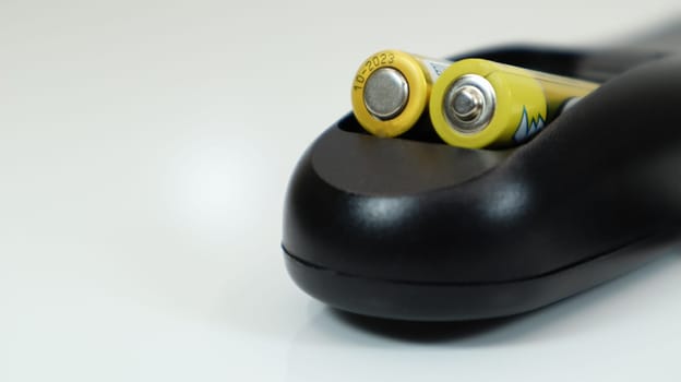 Black remote control with yellow AAA batteries on a white background. Battery replacement, spare parts. Remote control battery compartment close-up. Copy space.