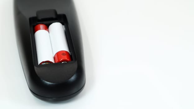 Black TV remote control with AAA alkaline batteries in red and white on a white background. Battery replacement, spare parts. Remote control battery compartment close-up. Copy space