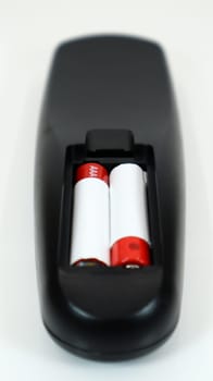Black TV remote control with AAA alkaline batteries in red and white on a white background. Battery replacement, spare parts. Remote control battery compartment close-up. Vertical photography