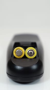 Black remote control with yellow AAA batteries on a white background. Battery replacement, spare parts. Remote control battery compartment close-up. Vertical photography.