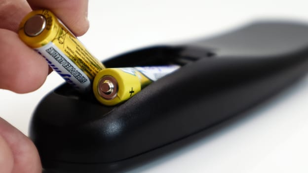 Insert the AAA size battery into the remote control. Installing batteries in the wireless device. A male hand holds a yellow alkaline battery. Text in English and Russian
