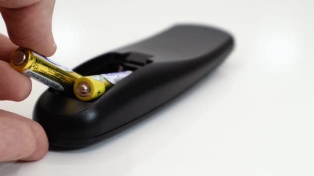 Insert the AAA size battery into the remote control. Installing batteries in the wireless device. A male hand holds a yellow alkaline battery. Text in English and Russian