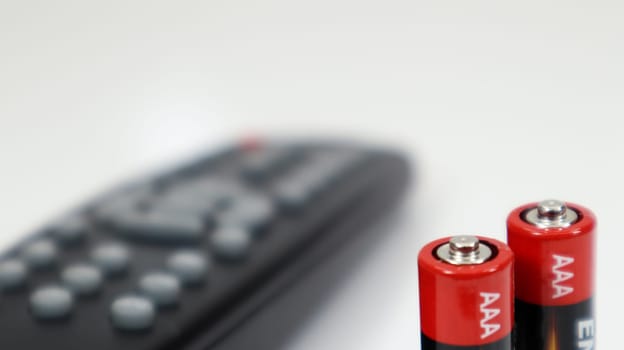 Black TV remote control with AAA alkaline batteries in red and white on a white background. Battery replacement, spare parts. Remote control battery compartment close-up