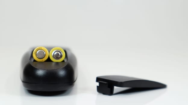 Black remote control with yellow AAA batteries on a white background. Battery replacement, spare parts. Remote control battery compartment close-up