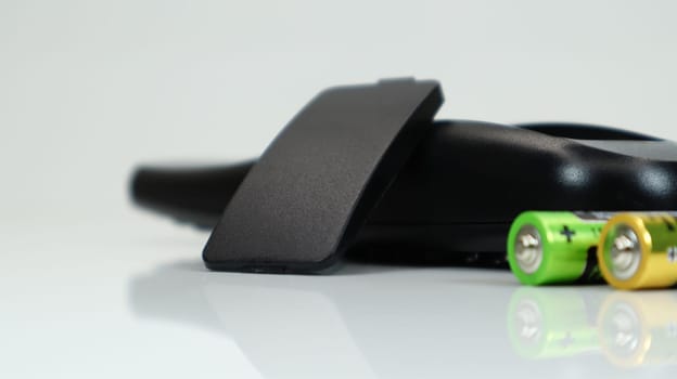 Black TV remote control with AAA alkaline batteries on a white background. Battery replacement, spare parts. Close up of the battery compartment of the remote control