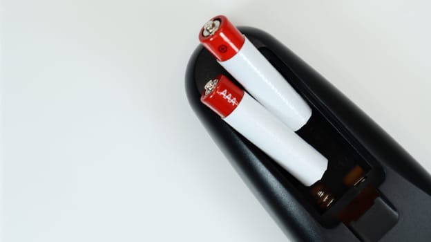 Black TV remote control with AAA alkaline batteries on a white background. Battery replacement, spare parts. Close up of the battery compartment of the remote control