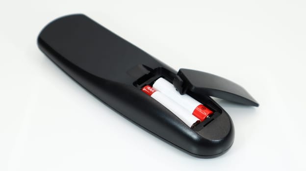 Black TV remote control with AAA alkaline batteries in red and white on a white background. Battery replacement, spare parts. Remote control battery compartment close-up