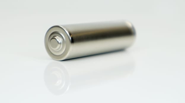 AA alkaline rechargeable battery on white glossy background with reflection. Close one empty battery with copy space
