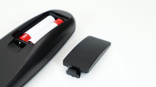 Black TV remote control with AAA alkaline batteries in red and white on a white background. Battery replacement, spare parts. Remote control battery compartment close-up. Copy space