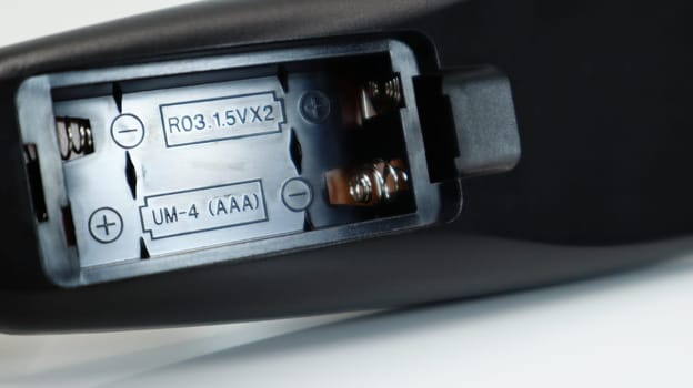 Black TV remote control with AAA alkaline batteries on a white background. Battery replacement, spare parts. Close up of an empty battery compartment of the remote control